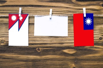 Hanging flags of Nepal and Taiwan attached to rope with clothes pins with copy space on white note paper on wooden background.Diplomatic relations between countries.