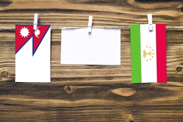 Hanging flags of Nepal and Tajikistan attached to rope with clothes pins with copy space on white note paper on wooden background.Diplomatic relations between countries.