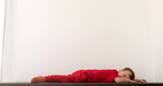 Child boy lying on the floor looking at the camera and turns away on white background