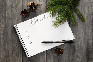 Planning new year. Notebook with to do list, Christmas tree branches and pinecones on wooden background top view