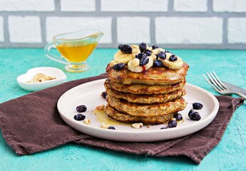 Banana oat pancakes with hazelnuts, sliced banana, honey and honeysuckle on a white plate on a...