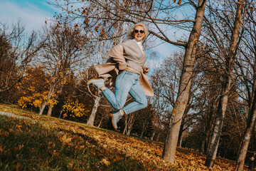 Fototapeta premium Beautiful woman in autumn park jumping and smiling - sunny day