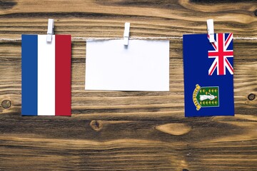 Hanging flags of Netherlands and British Virgin Islands attached to rope with clothes pins with copy space on white note paper on wooden background.Diplomatic relations between countries.