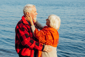 Fototapeta na wymiar cheerful senior citizens woman and man are standing and hugging on the lake, against the background of the bridge.