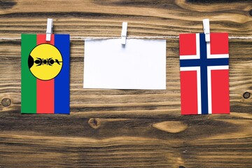 Hanging flags of New Caledonia and Norway attached to rope with clothes pins with copy space on...