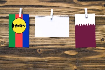 Hanging flags of New Caledonia and Qatar attached to rope with clothes pins with copy space on...