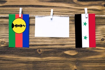 Hanging flags of New Caledonia and Syria attached to rope with clothes pins with copy space on...