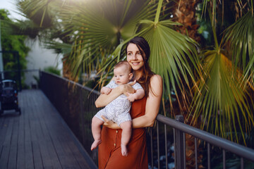 Proud Caucasian mother holding her adorable son while leaning on railing. In background are palm trees.