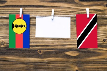 Hanging flags of New Caledonia and Trinidad And Tobago attached to rope with clothes pins with copy...