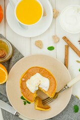 Stack of spicy pumpkin pancakes on a plate with honey and whipped cream on a white wooden background.  Rustic style. Fragrant autumn breakfast. Breakfast for Halloween.