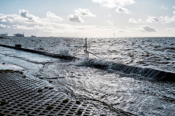 Splash of a wave on the flooded embankment near sea. It is written in german Please be careful. Steps can be slippery