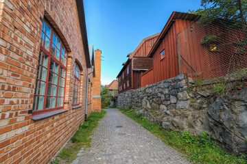 Fototapeta na wymiar Narrow cobblestone street between well-preserved red brick building and traditional red wooden dwelling houses on stone hill. Stockholm, Sweden.