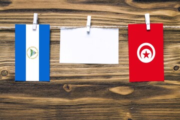 Hanging flags of Nicaragua and Tunisia attached to rope with clothes pins with copy space on white note paper on wooden background.Diplomatic relations between countries.