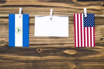 Hanging flags of Nicaragua and United States attached to rope with clothes pins with copy space on white note paper on wooden background.Diplomatic relations between countries.