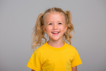 little blonde girl in yellow t-shirt smiling on light background, space for text