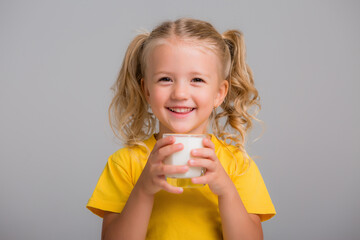 little blonde girl in yellow tank top holding a glass of milk on a light background, space for text