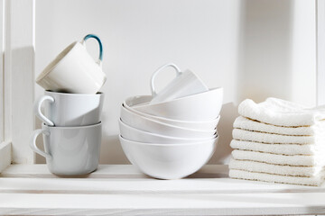 Fototapeta na wymiar Storage system in kitchen. Shelving with white mugs, bowls and towels
