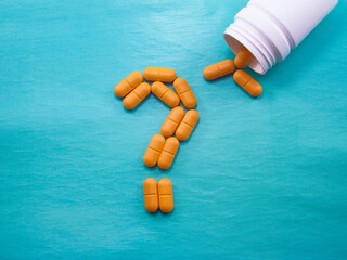 A lot of orange pills scattered on a blue background. A question mark laid out of pills....