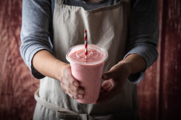 female with apron giving berry smoothie in plastic cup
