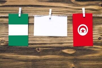 Hanging flags of Nigeria and Tunisia attached to rope with clothes pins with copy space on white note paper on wooden background.Diplomatic relations between countries.