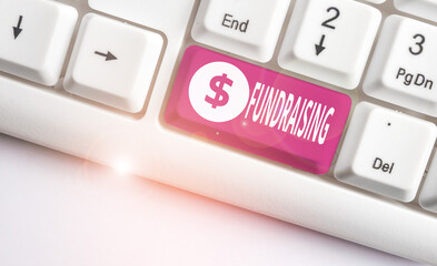 Conceptual hand writing showing Fundraising. Concept meaning seeking to generate financial support for charity or cause White pc keyboard with note paper above the white background