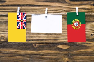 Hanging flags of Niue and Portugal attached to rope with clothes pins with copy space on white note paper on wooden background.Diplomatic relations between countries.