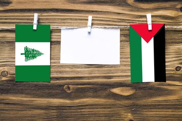 Hanging flags of Norfolk Island and Palestine attached to rope with clothes pins with copy space on white note paper on wooden background.Diplomatic relations between countries.
