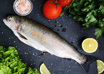 Fototapeta na wymiar Fresh trout with vegetables on a dark table