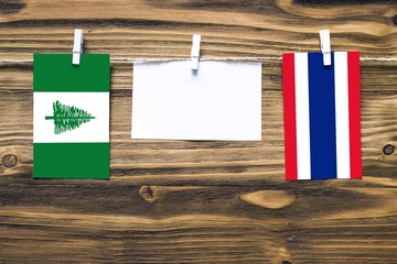 Hanging flags of Norfolk Island and Thailand attached to rope with clothes pins with copy space on...