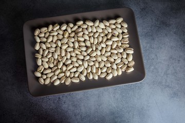 Pistachios nuts in brown plate on the dark background, captured from top