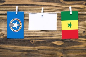 Hanging flags of Northern Mariana Islands and Senegal attached to rope with clothes pins with copy space on white note paper on wooden background.Diplomatic relations between countries.