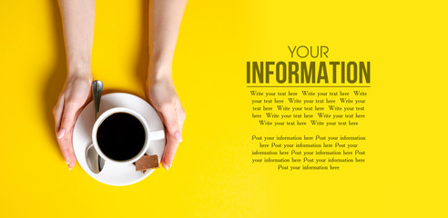 Cup of coffee with chocolate pieces in hand on yellow background, top view, space for text