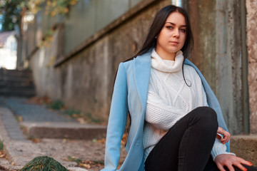 Beautiful girl on the street sits in a coat. Green eyes. Autumn coat