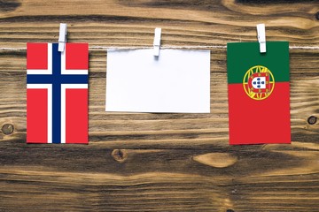 Hanging flags of Norway and Portugal attached to rope with clothes pins with copy space on white note paper on wooden background.Diplomatic relations between countries.