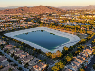 Aerial view of water recycling reservoir surrounded by suburban neighborhood with big villas during sunset time, South California