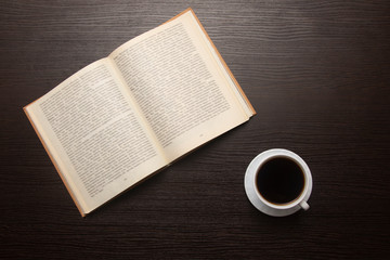 open book and cup of coffee on a wooden dark table