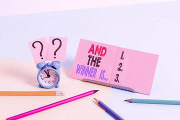 Conceptual hand writing showing And The Winner Is. Concept meaning announcing a demonstrating or thing that wins something Mini size alarm clock beside stationary on pastel backdrop