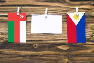 Hanging flags of Oman and Philippines attached to rope with clothes pins with copy space on white note paper on wooden background.Diplomatic relations between countries.