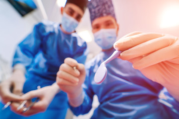 Obraz na płótnie Canvas Two male dentists in uniform give dental treatment to a patient at dentistry office. View through the eyes of the client. Closeup.