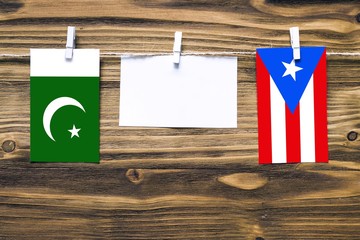 Hanging flags of Pakistan and Puerto Rico attached to rope with clothes pins with copy space on white note paper on wooden background.Diplomatic relations between countries.