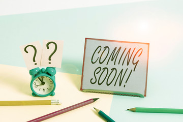 Conceptual hand writing showing Coming Soon. Concept meaning event or action that will happen after really short time Mini size alarm clock beside stationary on pastel backdrop