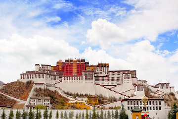 Front view of the Potala Palace in Lhasa, Tibet, surrounded by green vegetation, against a blue summer sky covered by white clouds.