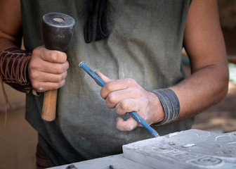 man's hands working with hammer and chisel in craft workshop.