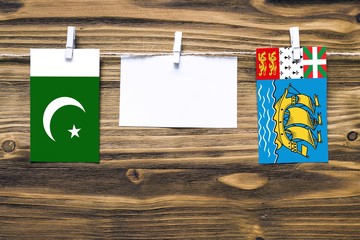 Hanging flags of Pakistan and Saint Pierre And Miquelon attached to rope with clothes pins with copy space on white note paper on wooden background.Diplomatic relations between countries.