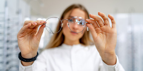 Happy female client or optician is standing with set of glasses in background in optical shop. Woman in spectacles. Girl wearing glasses. Portrait of a woman in correcting glasses. Closeup.