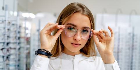 Happy female client or optician is standing with set of glasses in background in optical shop....
