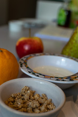 Close-up of a bowl filled with homemade granola on a breakfast table with yoghurt and fresh fruit. Healthy, organic ingredients.