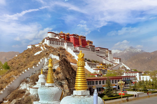 Lateral view of the Potala Palace in Lhasa, Tibet, surrounded by green vegetation, against a blue summer sky covered by white clouds.
