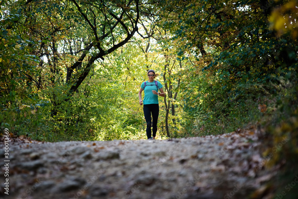 Wall mural active woman with sunglasses approaching running on a trail in the nature