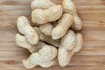 A pile of unshelled peanuts in the center on a brown wooden surface, top view